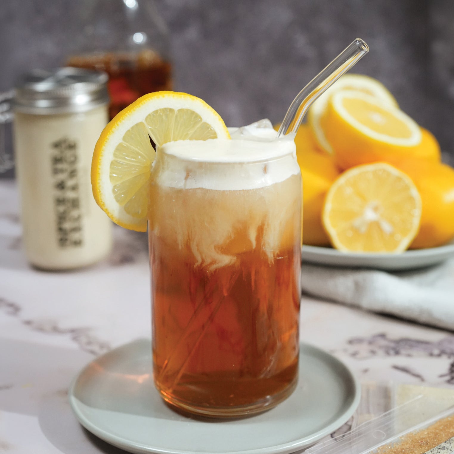 Glass of iced tea with lemon slices and whipped cream topping on a table.